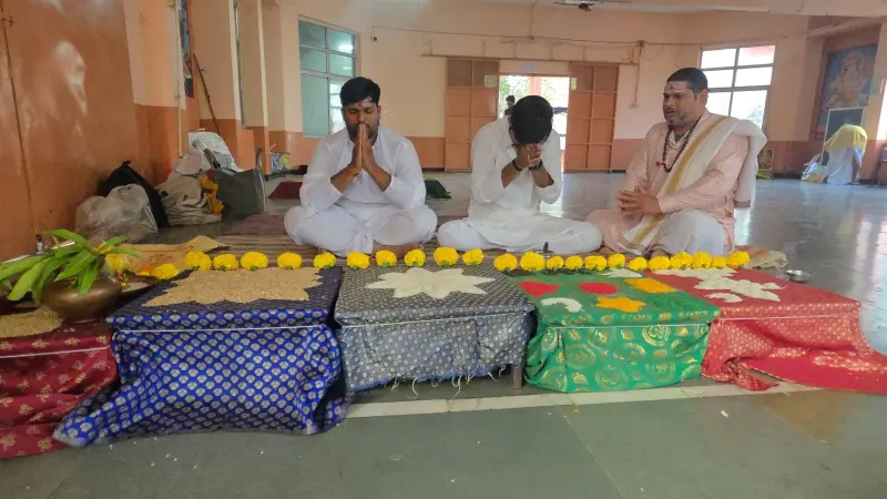 Devotees seated in a row for the puja, samagri arranged on coloured cloth